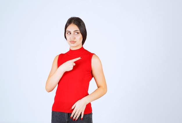 Chica con una camisa roja apuntando hacia el lado derecho.