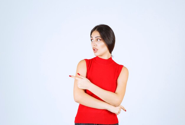 Chica con una camisa roja apuntando hacia el lado izquierdo.