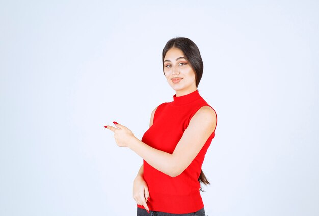 Foto gratuita chica con una camisa roja apuntando hacia el lado izquierdo.