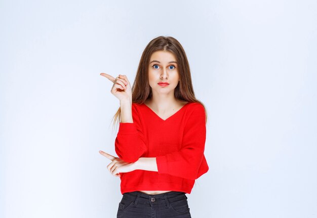 Chica con camisa roja apuntando hacia el lado izquierdo.