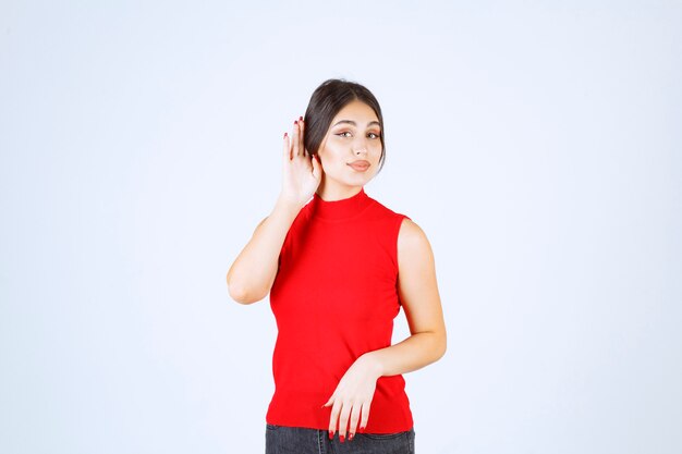 Chica de camisa roja apuntando a su oído para escuchar bien.