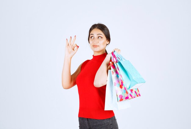 Chica en camisa roja con bolsas de colores detrás de su hombro.