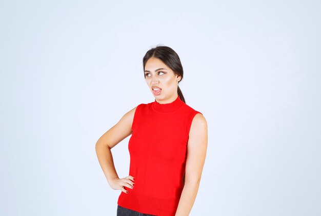 Chica en camisa roja haciendo cara molesta y aburrida.