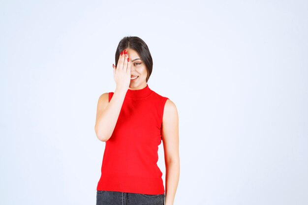 Chica de camisa roja mirando a través de sus dedos.