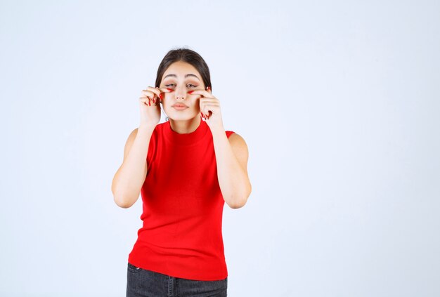 Chica de camisa roja mirando a través de sus dedos.