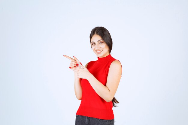 Chica con camisa roja mostrando algo a la izquierda.