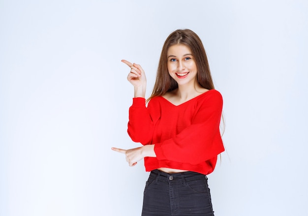 Chica con camisa roja mostrando algo en el lado izquierdo.