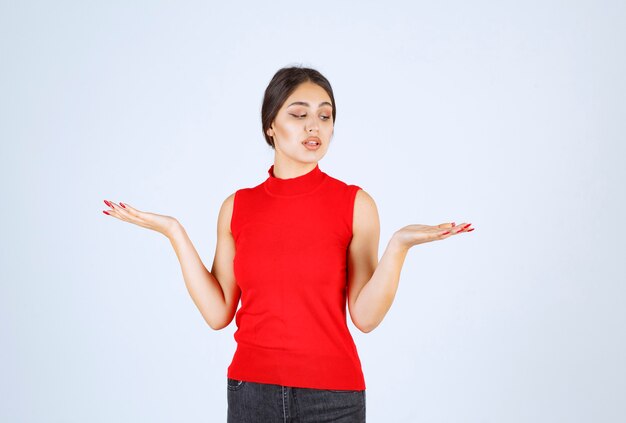 Chica en camisa roja mostrando algo en su mano abierta.