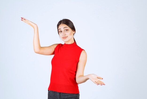 Chica en camisa roja mostrando algo en su mano abierta.