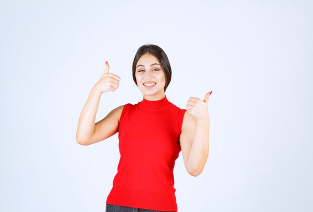 Chica en camisa roja mostrando signo de mano de disfrute.