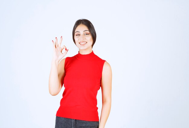 Chica en camisa roja mostrando signo de mano de disfrute.