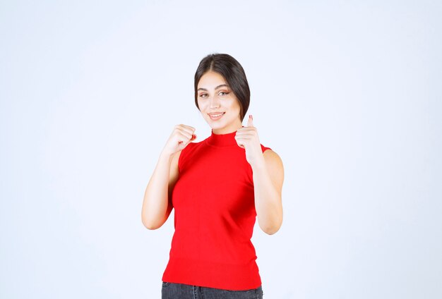 Chica en camisa roja mostrando signo de mano de disfrute.