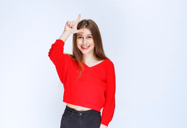 Chica en camisa roja mostrando signo de perdedor en su frente.