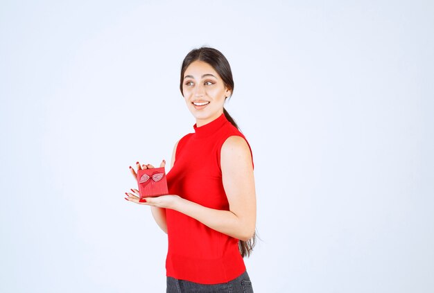 Chica en camisa roja mostrando su caja de regalo roja.