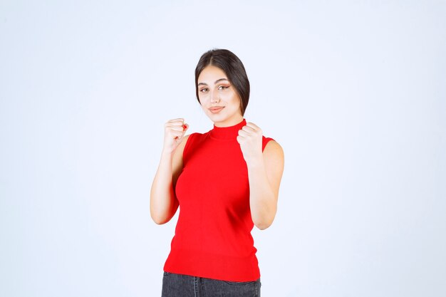 Chica en camisa roja mostrando sus puños y músculos del brazo.