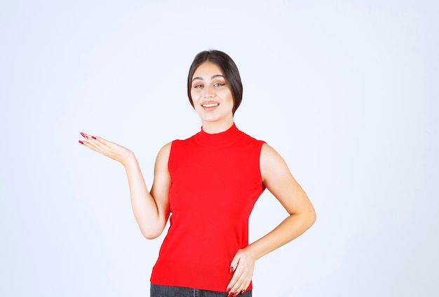Chica en camisa roja presentando y mostrando algo en su mano.