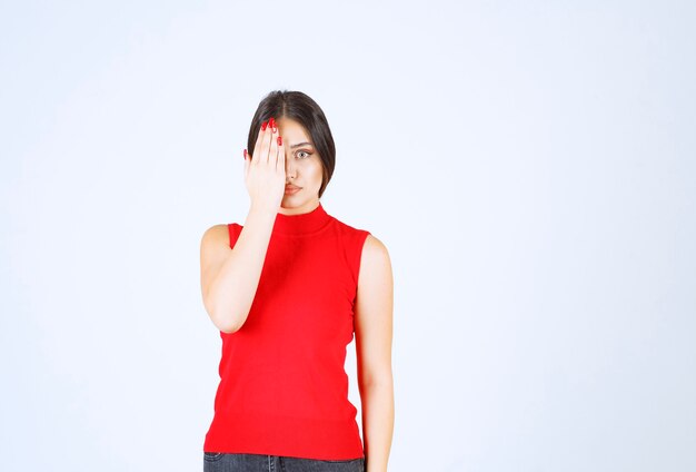 Chica en camisa roja que cubre parte de su rostro con la mano.