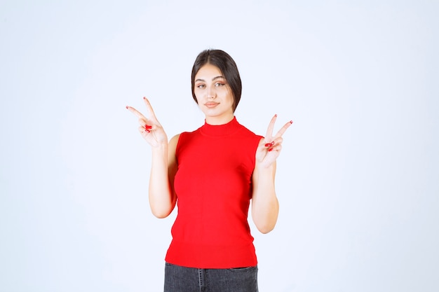 Chica en camisa roja que muestra el signo de la paz y la amistad.