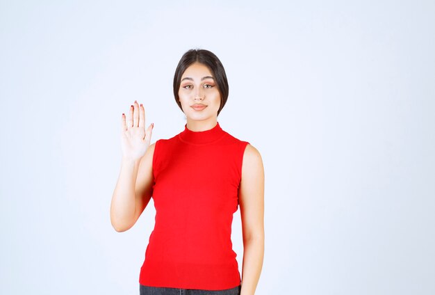 Chica en camisa roja saludando o invitando a alguien.