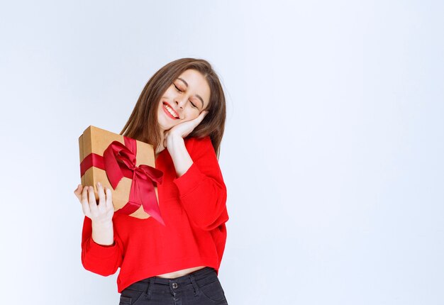 Chica en camisa roja sosteniendo una caja de regalo de cartón envuelta con cinta roja.