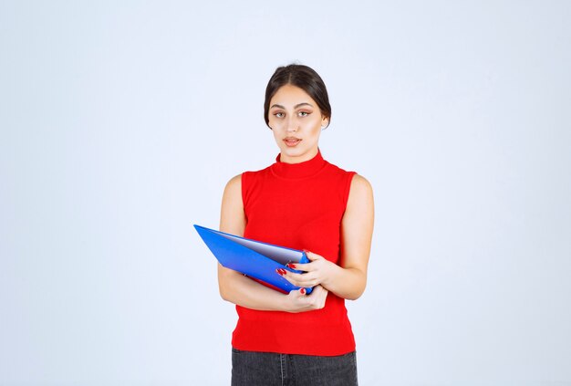 Chica de camisa roja sosteniendo una carpeta de negocios azul.