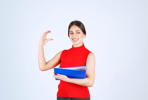 Chica de camisa roja sosteniendo una carpeta de negocios azul.