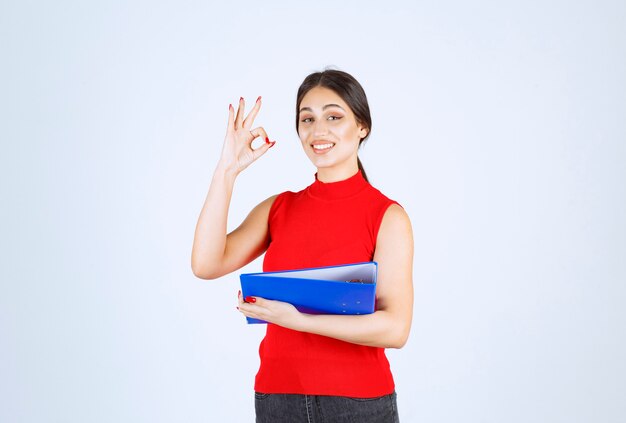 Chica de camisa roja sosteniendo una carpeta de negocios azul.