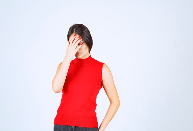 Chica de camisa roja sosteniendo su cabeza con las manos ya que tiene dolor de cabeza.