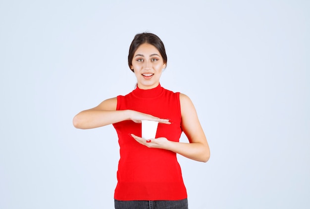 Chica con una camisa roja sosteniendo una taza de café con leche entre las manos.