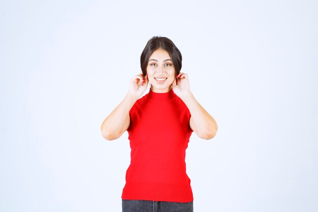 Chica con una camisa roja tirando de sus orejas en señal de mala suerte.