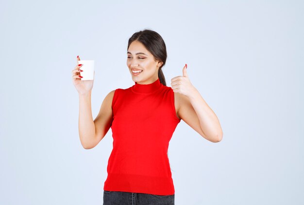 Chica en camisa roja tomando café y mostrando signos positivos.