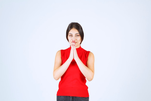 Chica de camisa roja uniendo las manos y rezando.