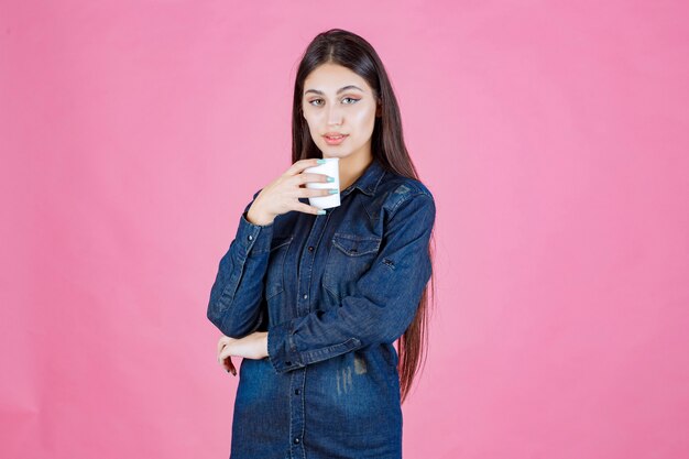 Chica en camisa vaquera disfrutando de una taza de café desechable