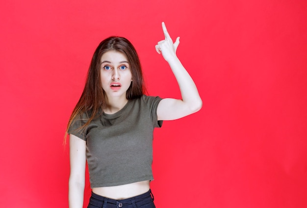 Chica en camisa verde apuntando a algo arriba.