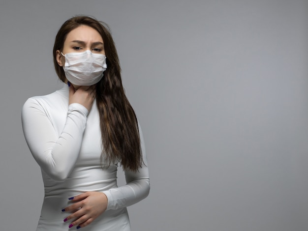 Chica en camiseta blanca sosteniendo su garganta con máscara protectora blanca