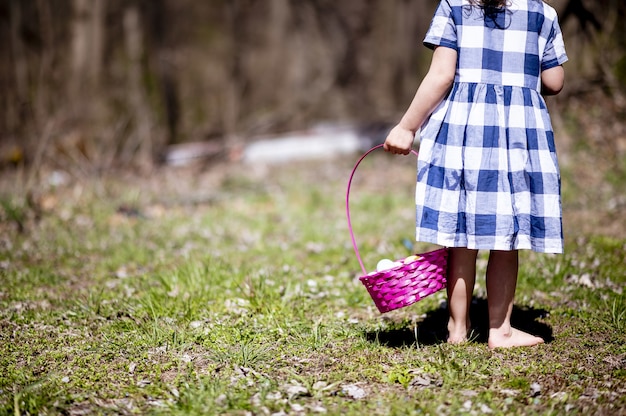 Chica con una canasta de coloridos huevos de Pascua sobre la hierba verde en un campo