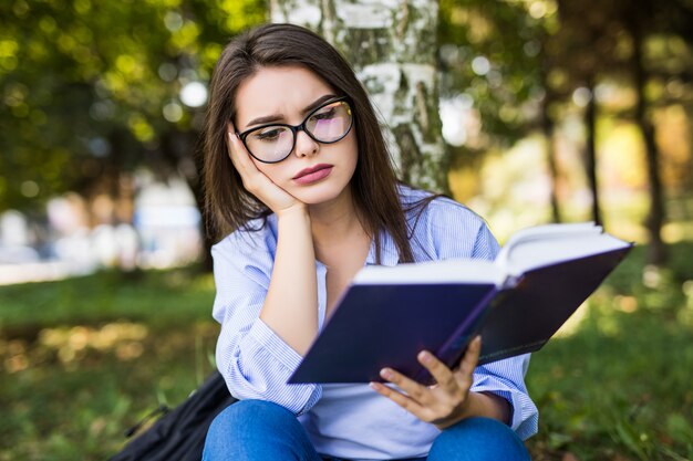 Chica cansada en estudios de chaqueta y gafas de jeans en el parque verde de verano.