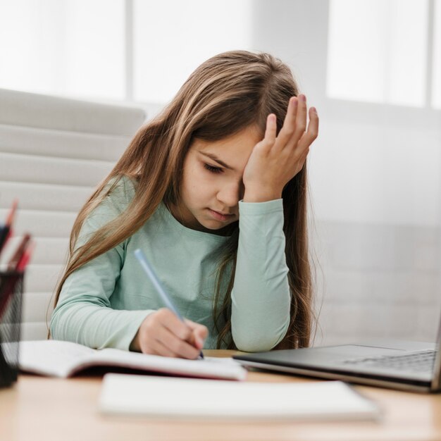 Chica cansada tomando notas en casa