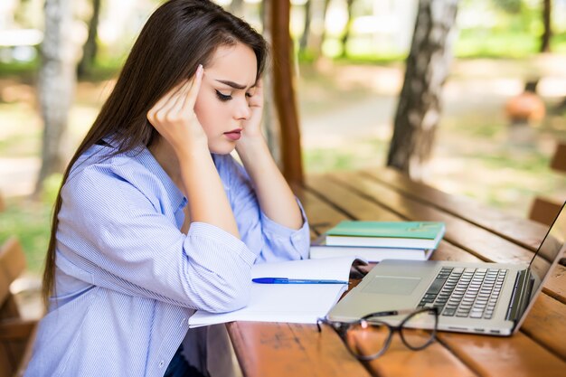 Chica cansada usando una computadora portátil en una mesa del parque al final del día