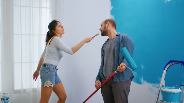 Chica cantando en el pincel y decorando el apartamento con la ayuda de un marido alegre. Redecoración de apartamentos y construcción de viviendas mientras se renueva y mejora. Reparación y decoración.