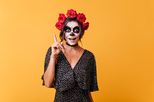 La chica con la cara pintada para Halloween tiene una nueva idea divertida. Retrato de mujer joven con estilo con rosas en el pelo.