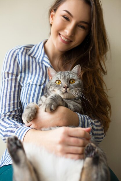 Chica cariñosa abrazando a su gato en casa cerca de la ventana Chica alegre sosteniendo a su mascota sorprendida Chica ama a su gato Amigos expresando sentimientos