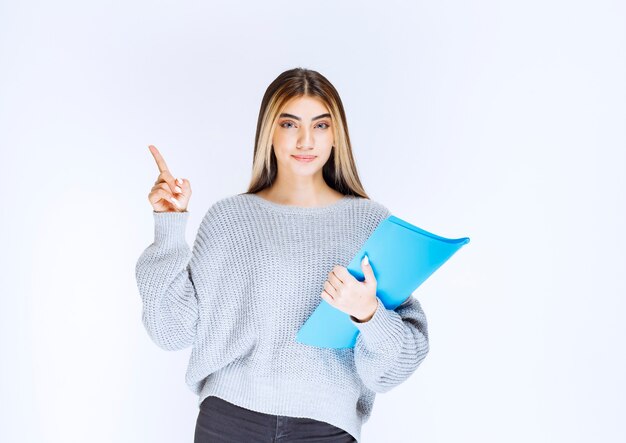 Chica con una carpeta azul apuntando a alguien a un lado.