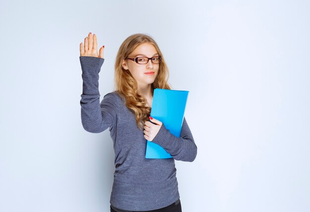 Chica con una carpeta azul levantando la mano para llamar la atención.