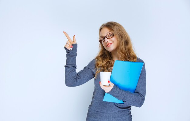 Chica con una carpeta azul sosteniendo una taza de café desechable.