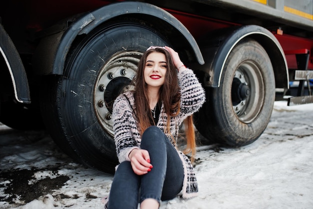 Foto gratuita chica casual elegante morena con gorra sentada contra ruedas de camión