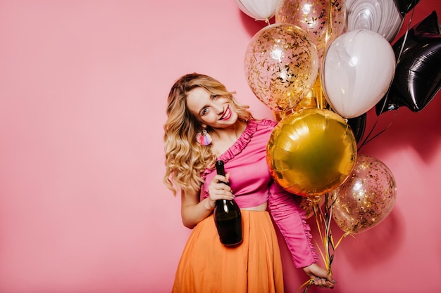 Chica caucásica alegre sonriendo durante el rodaje de la fiesta Mujer joven rizada posando en el estudio con globos