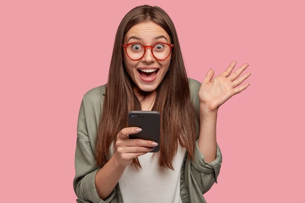 Chica caucásica asombrada sostiene teléfono celular moderno y muestra la palma
