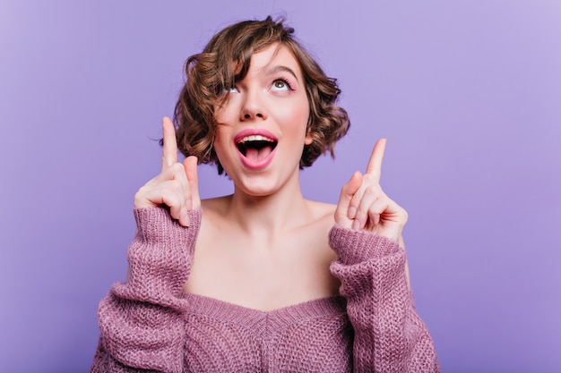 chica caucásica curiosa mirando hacia arriba. Foto interior del modelo femenino de ensueño aislado en la pared púrpura y sonriendo.