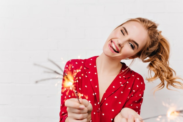 Chica caucásica expresando emociones positivas y agitando bengalas. Maravillosa señorita riendo esperando año nuevo con luces de bengala.